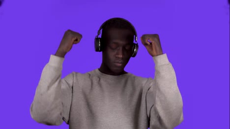 Pleased-african-man-in-white-shirt-and-headphones-dancing-relaxfuly-with-eyes-closed-over-blue-background.-Slow-motion