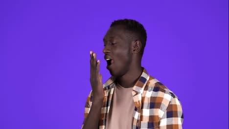 A-short-haired-young-african-american-man-is-yawning,-touching-his-face,-tired-and-sleepy-standing-isolated-over-blue-wall-background-in-studio.-Side-view