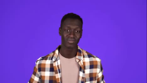 Happy,-smiling-african-american-man-in-good-mood-on-blue-background.-Gesturing-with-thumbs-up,-like-gesture,-touching-his-plaid-shirt---human-emotions