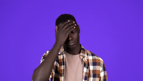 Portrait-of-dark-skinned-young-man-rolling-his-eyes-up-isolated-on-blue-background.-Selfish-man-in-plaid-shirt-tired