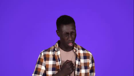Sick-young-African-Man-coughing-hard-and-hitting-himself-the-chest-isolated-on-blue-background.-Wearing-plaid-shirt