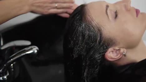 Hairdresser-washing-long-haired-woman-and-massaging-shampoo-into-scalp-before-haircut.-Hairdresser's-hands-wash-head-applying,-foaming-the-shampoo-on-head.-Close-up