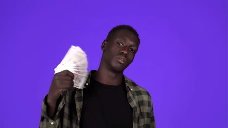 Happy-african-american-man-holding-hundred-dollar-banknotes-fan,-nodding-head-and-looking-at-camera-while-posing-against-blue-background-in-studio