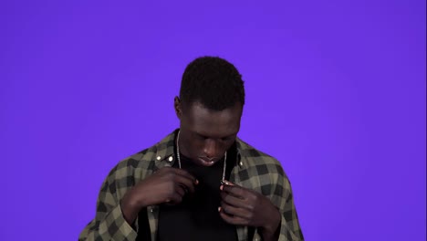 African-american-guy-portrait-on-blue-background.-Wealth,-vanity,-pride,-arrogance.-Guy-in-casual-trying-to-close-the-golden-chain-on-his-neck