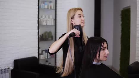 Caucasian-brunette-young-woman-get-her-hair-dry-by-beautician-barber-after-before-the-new-haircut-in-hairdresser-salon.-Beauty-industry.-Slow-motion