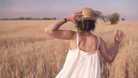 Tracking-footage-of-a-beautiful-girl-in-white-summer-dress-and-straw-hat-running-freely-by-wheat-field.-Backside-view