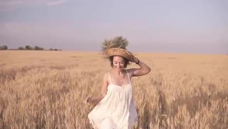 Gorgeous-young-woman-in-white-dress-runnung-in-the-wheat-field.-Smiling,-happy-female-running-and-holds-her-straw-hat-on-her-head.-Front-view