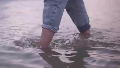 Close-up-footage-of-a-young-woman's-feet-walking-by-water,-lake-in-blue-jeans.-Daytime,-summer