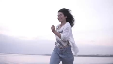 Young,-happy,-cheerful-brunette-girl-happily-running-by-seaside-in-casual-clothes.-Freedom,-healthy-lifestyle