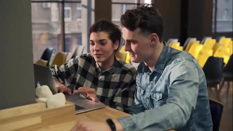 Couple-of-two-young-attractive-people-sitting-in-front-of-laptop-talking-about,-discussing-something.