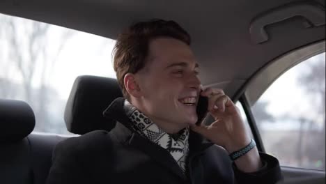 Attractive-sexy-guy-in-black-stylish-coat-is-smiling-while-talking-to-someone-on-the-phone-in-a-car.