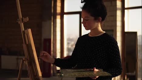 Fully-concentrated-sophisticated-female-artist-in-her-20's-is-drawing-picture-on-easel.-Slow-motion-rotating-fotage.