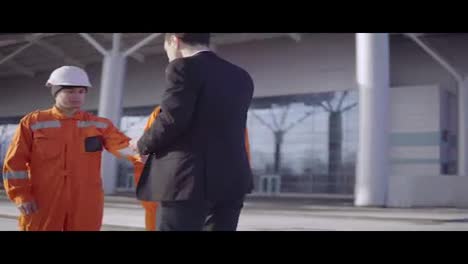 Manager-in-a-suit-giving-envelopes-with-money-to-workers-in-orange-uniform-and-helmets.-Successful-finish-of-the-project.-Shot-in-4K