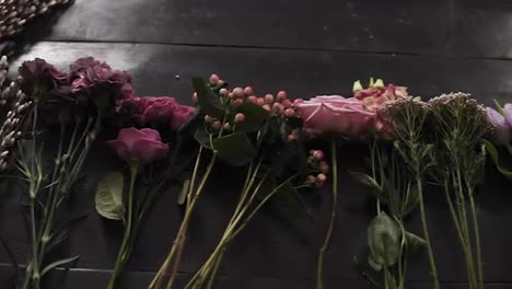Medium-close-up-footage-of-a-colorful-variety-of-flowers-in-bloom-exposed-in-a-row-on-a-dark-wooden-surface