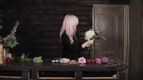 A-pretty-girl-florist-on-a-dark-background-makes-a-composition-of-flowers.-Modern,-wooden-interior