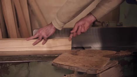 Man-in-overalls-polish-and-align-boards-with-electric-saw,-in-a-carpentry-workshop.-Slow-motion