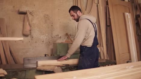 The-carpenter-cuts-off-the-sides-of-the-wood-block-on-the-circular-saw.-Wooden-shavings.-The-workshop-is-filled-with-wooden-products