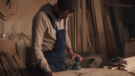 The-carpenter-in-his-small-workshop-is-working-on-polishing-the-piece-of-wood.-Sander.-Aiming-shooting