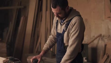 A-footage-of-a-carpenter-working-in-overalls.-A-man-grinding-a-wood-in-a-carpentry-shop.-Slow-motion