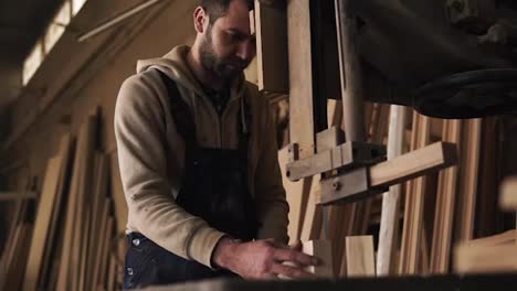 The-young-carpenter-is-extremely-concentrated-on-working-with-the-electric-saw.-Works-with-small-bars.-Timber-on-the-background