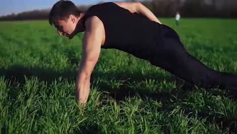 The-young-guy-assiduously-does-push-ups-on-one-hand.-Complicated.-Beautiful-nature,-meadow,-clear-sky.-Overview-footage