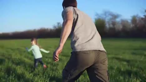 Happy-family-having-a-rest-on-a-meadow-on-a-sunny-day.-Father-plays-catch-up-with-his-little-daughter.-Wide-green-field.-Young-caucasian-family.-Chasing-footage