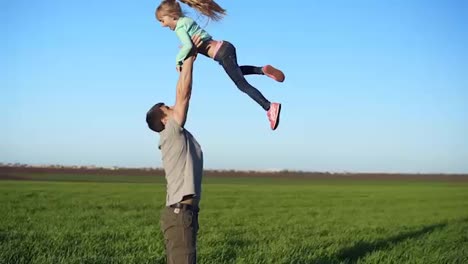 Slow-motion-of-handsome-young-father-throwing-his-adorable-daughter-in-the-air.-Active-life.-Beautiful-green-field