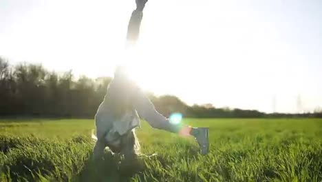 Front-view-of-a-beautiful-young-girl-doing-somersault-outside-on-the-green-field.-Enjoys-her-time.-Sunny-day.-Smiling.-Slow-motion