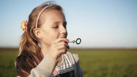 Cute-little-girl-is-blowing-soap-bubbles-in-the-meadow-on-a-sunny-day.-Slow-Motion.-Happy-childhood.-Blurred-background