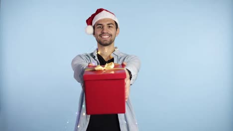 Young-man-wearing-Christmas-Santa-hat-and-garland-on-neck-holding-gift-over-isolated-blue-background-with-outstretched-hands-with-a-happy-face-standing-and-smiling-with-a-confident-smile-showing-teeth