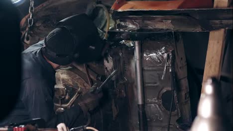 Backside-footage-of-a-welder-joining-some-metal-pieces-together-on-car's-bottom-surface-with-a-welding-torch.