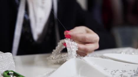 Nahaufnahme-Weiblicher-Hände-Mit-Rosa-Maniküre,-Die-Nadel-Und-Faden-Halten-Und-Ein-Exklusives-Hochzeitskleid-Mit-Dekorativen-Steinen-Dekorieren.-Nähen-Eines-Eleganten-Hochzeitskleides.-Handgemacht