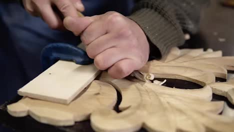 Carpenter-working-on-a-wooden-in-his-workshop-on-the-table,-preparing-a-detail-of-wooden-product,-a-part-of-future-furniture.-Close-up-footage-of-a-man's-hands-cuts-out-patterns-with-a-planer