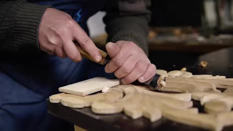 Slow-motion-of-carpenter-working-on-a-wooden-in-his-workshop-on-the-table,-preparing-a-detail-of-wooden-product,-a-part-of-future-furniture.-Close-up-footage-of-a-man's-hands-cuts-out-patterns-with-a-planer