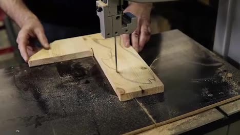Close-up-footage-of-male's-hands-working-with-an-electric-cutting-machine.-High-angle-footage-of-a-man-cutting-a-fish-shape-wooden-pattern-on-a-table