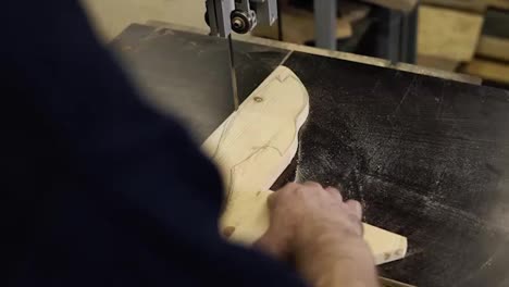 Close-up-footage-of-male's-hands-working-with-an-electric-cutting-machine.-High-angle-footage-of-a-man-cutting-a-fish-shape-wooden-pattern-on-a-table.-Footage-from-the-shoulder