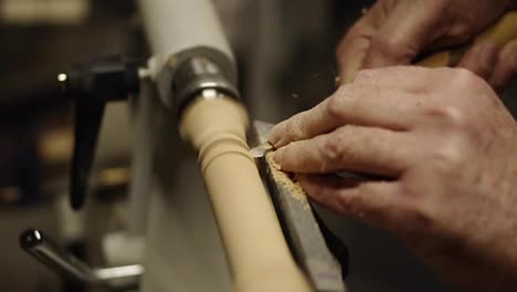 Carpenter-male-hands-cutting-wooden-knob-out-of-wood-piece-spinning-on-machine-using-chisel,-close-up-shot.-Slow-motion