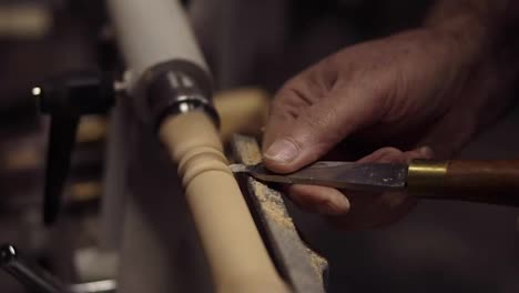 Carpenter-male-hands-cutting-wooden-knob-out-of-wood-piece-spinning-on-machine-using-chisel,-close-up-shot.-Slow-motion.-Side-view