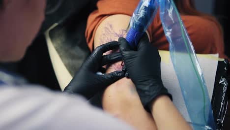Close-up-female-tattoo-artist-holding-tattoo-gun-working-on-hand-tattoo.-Gloved-hand-holding-tattoo-gun-working-on-modern-body-art.-Artist-working-on-female's-hand.-Slow-motion