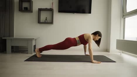 Young-sporty-woman-is-doing-push-ups-exersice-on-mat-in-living-room