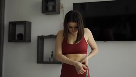 Fitness-woman-in-sportswear-measures-waist-circumference-with-tape-in-the-kitchen,-feels-upset