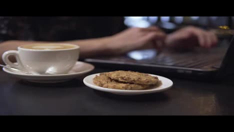 Tasse-Kaffee-Und-Kekse.-Frau-Arbeitet-Mit-Laptop-Im-Hintergrund