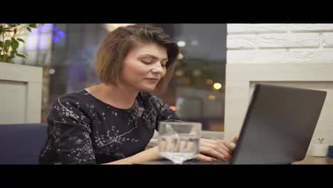 Mujer-De-Negocios-Joven-Sentada-En-Un-Café-Con-Una-Computadora-Portátil,-Trabajando-Y-Bebiendo-Agua