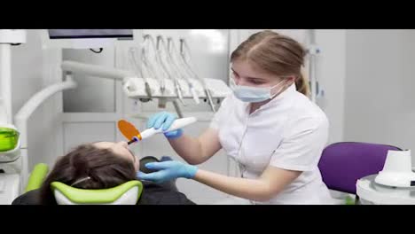 Young-female-dentist-in-mask-and-gloves-using-dental-UV-light-equipment-for-polymer-hardening