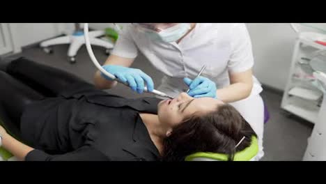 Young-female-dentist-in-gloves-and-mask-drilling-patient's-teeth-in-clinic
