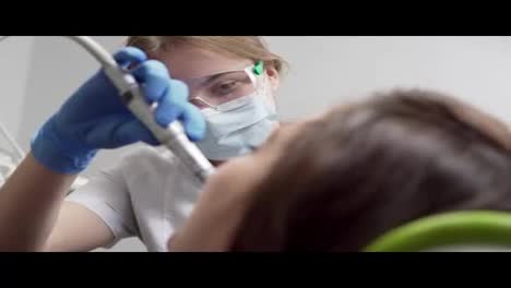 Young-female-dentist-in-gloves-and-mask-drilling-patient's-teeth-in-clinic