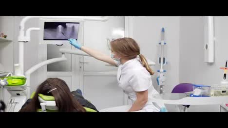 Healthy-teeth-and-dental-healthcare.-Confident-professional-doctor-dentist-is-showing-x-ray-teeth-on-a-tablet.-Female-dentist-in-mask-and-lab-coat.