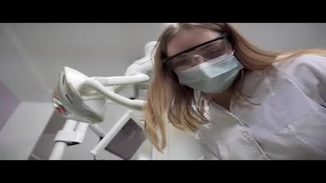 Young-female-dentist-in-mask-examining-patient-using-tools,-Standing-Upon-a-Patient,-Looking-at-Camera,-Dentist's-Face