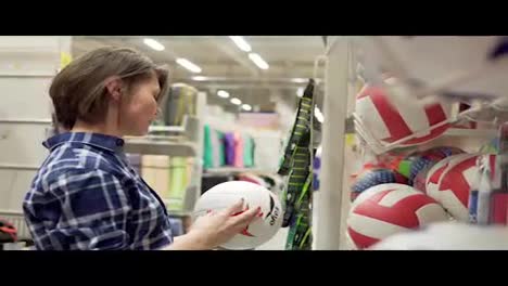 Young-woman-selecting-sport-equipment-in-supermarket.-Choosing-ball-for-soccer-or-football
