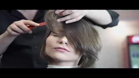 Professional-hairdresser,-stylist-combing-hair-of-female-client-and-using-barrette-for-fixing-hairdo-in-professional-hair-salon.-Beauty-and-haircare-concept